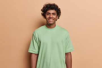 Studio waist up of young happy smiling Hindu man with black curly short hair standing in centre...