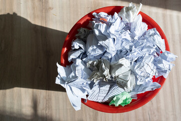 Full trash bin with crumpled paper scattered around