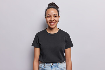 Waist up shot of cheerful Latin woman with combed hair and pleasant smile on face dressed in casual black t shirt annd jeans concentrated at camera isolated on white background. Happy face expressions