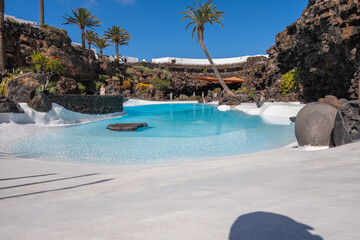 Pool of blue waters and palemeeras, outside the cave of Los Jameos del Agua. Light at the end of the cave. Sky with big white clouds. Lanzarote, Canary Islands, Spain.