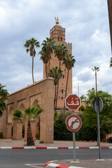 Photo of the tower of the Koutoubia Mosque. In the photo there is a stop sign written in Arabic. Cloudy day.