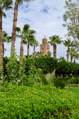 Photo of the upper part of the tower of the Koutoubia mosque in the city of Marrakech, tower covered by trees and palm trees. Cloudy day.