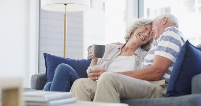 Love, happy and senior couple hug on a sofa with coffee, connection and romance at home together. Support, gratitude and old people embrace in a living room enjoying relationship, tea and retirement