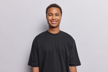 Horizontal shot of satisfied shaved African man with curly hair broad smile on face looks directly at camera dressed in casual black t shirt isolated over white background glad to hear good news
