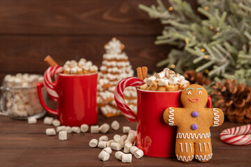 Fototapeta premium Hot drink with marshmallows and candy cane in a red cup on a texture table.Cozy seasonal holidays.Hot cocoa with gingerbread Christmas cookies.Hot chocolate with marshmallow and spices.Copy space.