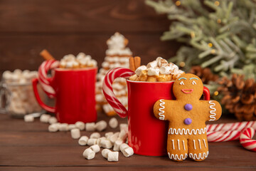 Hot drink with marshmallows and candy cane in a red cup on a texture table.Cozy seasonal holidays.Hot cocoa with gingerbread Christmas cookies.Hot chocolate with marshmallow and spices.Copy space.