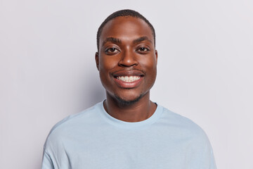 Portrait of happy dark skinned man smiles toothily looks directly at camera has cheerful expression...