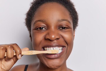 Close up shot of dark skinned African woman with short curly hair brushing teeth with toothbrush...