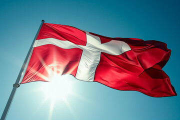 Danish flag against the sun in a clear sky.
