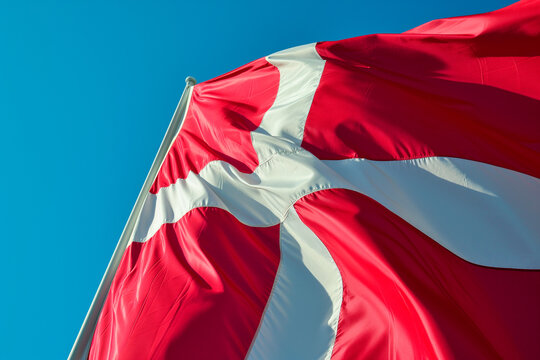 Danish flag against the sun in a clear sky.
