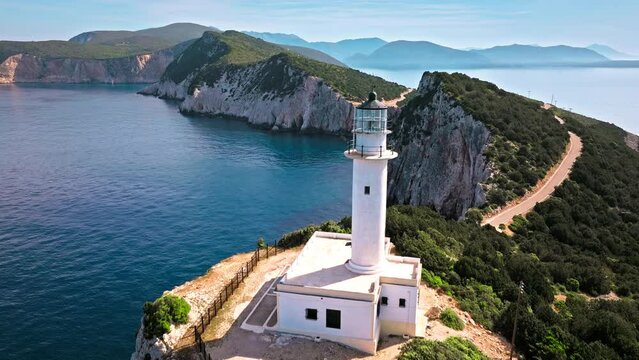 Aerial view of Phare de Akrotiri Lefkada Lighthouse in Cape Doukato. View from above of a white tower on a rocky cliff by the edge of the coast in Lefkada surrounded by emerald-blue waters.