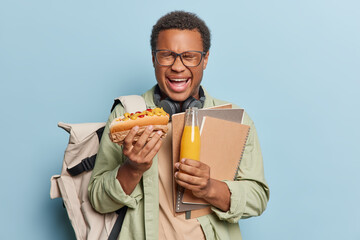 Emotional dark skinned African man poses with hotdog bottle of fresh orange juice and notepads...