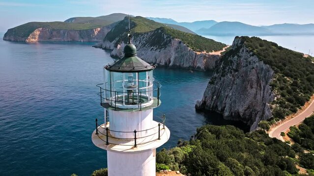 Aerial view of Phare de Akrotiri Lefkada Lighthouse in Cape Doukato. View from above of a white tower on a rocky cliff by the edge of the coast in Lefkada surrounded by emerald-blue waters.