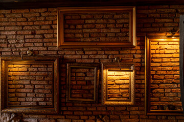 Vintage picture frames hanging on a red brick wall and illuminated by lamps