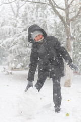 Fototapeta na wymiar a girl is playing with snow on the street, it is snowing, a blizzard and frost on a winter day