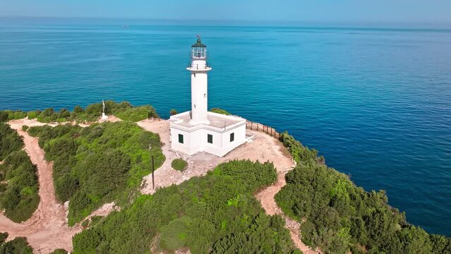 Aerial view of Phare de Akrotiri Lefkada Lighthouse in Cape Doukato. View from above of a white tower on a rocky cliff by the edge of the coast in Lefkada surrounded by emerald-blue waters.