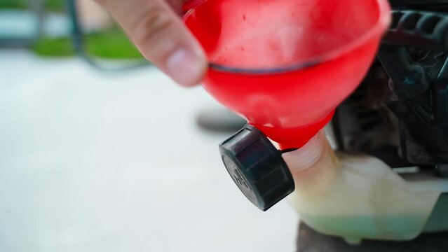 Gasoline Oil mixture is poured through a funnel into the gas tank of a gasoline trimmer close-up. Refilling the trimer with a blue fuel-oil mixture