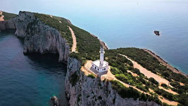 Aerial view of Phare de Akrotiri Lefkada Lighthouse in Cape Doukato. View from above of a white tower on a rocky cliff by the edge of the coast in Lefkada surrounded by emerald-blue waters.