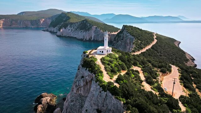 Aerial view of Phare de Akrotiri Lefkada Lighthouse in Cape Doukato. View from above of a white tower on a rocky cliff by the edge of the coast in Lefkada surrounded by emerald-blue waters.