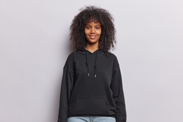 Waist up shot of curly haired teenage girl smiles happily dressed in casual black sweatshirt jeans...