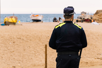 A police officer stands guard on the beach during his work day. The agent has his back turned,...