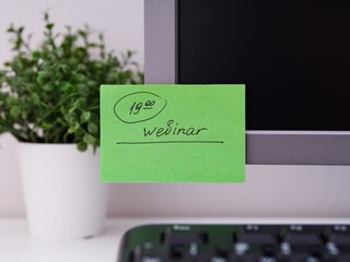 A green paper notes with the reminder 19-00 Webinar on it sticked on to a monitor at an office...