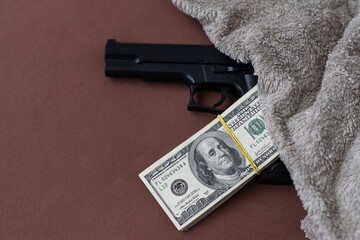 Pile of US dollar cash and a black pistol gun. Seen from above.