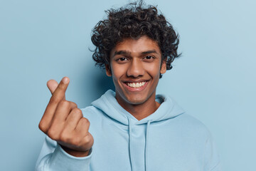 Happy Hindu man shows mini heart gesture shapes korean like sign smiles pleasantly expresses love...