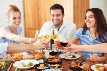 Hands with white wine toasting over served table with food