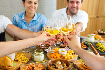 People with white wine toasting over served table with food.