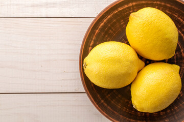 Three yellow ripe lemons on a plate of clay on a wooden table, close-up, top view.