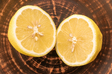 Two halves of a yellow juicy lemon on a clay dish, close-up, top view.