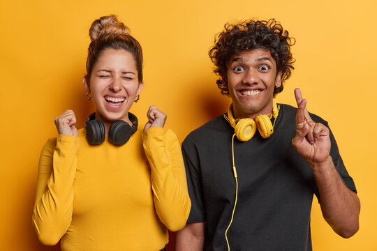 People And Happiness. Studio Waist Up Of Young Happy Smiling Excited European Woman And Hindu Guy Standing Close To Each Other On Yellow Background Wearing Casual Clothes With Headphones On Neck