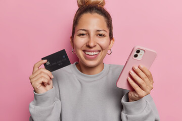 Easy payments. Cheerful young woman holds credit card and smartphone enjoys mobile shopping...