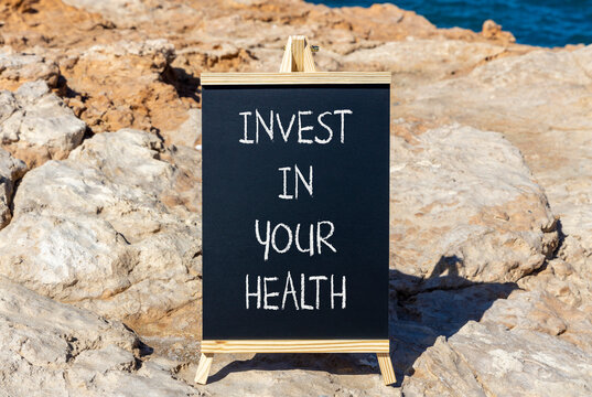 Invest in your health symbol. Concept word Invest in your health on beautiful black chalk blackboard. Beautiful red stone blue sea background. Invest in your health concept. Copy space.