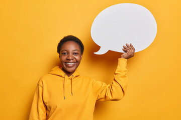 Positive dark skinned teenage girl smiles toothily holding speech bubble with empty space for text...