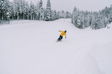 Snowboarder in a yellow ski suit rides a snowboard leaning to the side from a snowy mountain