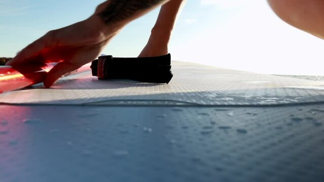 a girl in a yellow swimsuit sits on a SUP on the water and removes the safety rope for the SUP board from her leg