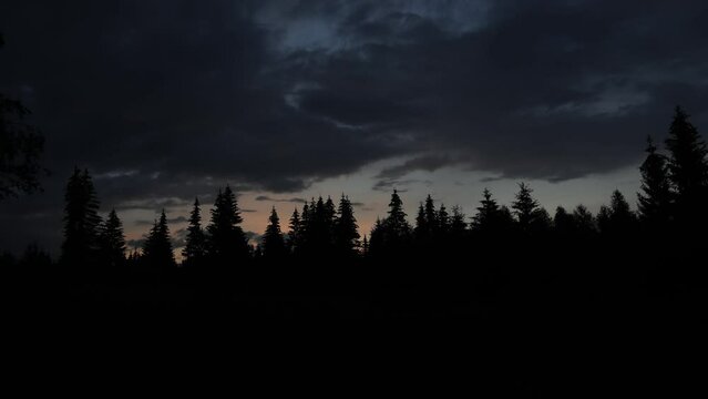 4k movie sunset timelapse with moving clouds over forest and mountains with spruce tree forest silhouette after sunset.