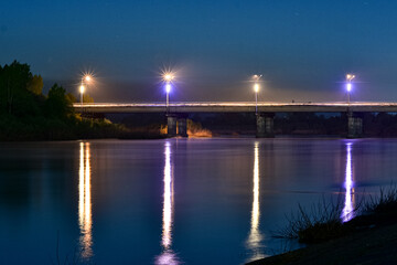 Fototapeta premium Night landscape. Road bridge over the river at night.