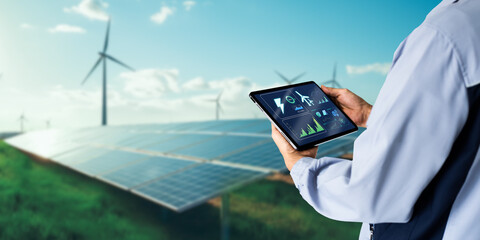 Sustainable energy management system concept.Engineer using digital tablet with wind turbine and solar panels powerplant as background - obrazy, fototapety, plakaty