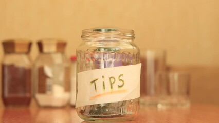 Man putting tips into glass jar on wooden table