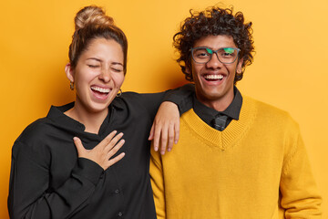 Cheerful woman and man laughs joyfully at something funny have fun together express positive emotions feel free and happy stand next to each other isolated over yellow background. Friendship concept
