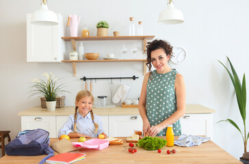 Beautiful brunette mother and her daughter packing healthy lunch and preparing school bag