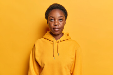 Portrait of beautiful dark skinned woman concentrated at camera has serious expression dressed in...