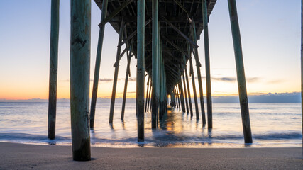 Sunrise casts a warm glow over Kure Beach pier, with soft waves lapping the shore in North Carolina.