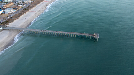 Kure Beach Pier extends into the Atlantic Ocean, captured from above during a serene North Carolina sunrise.
