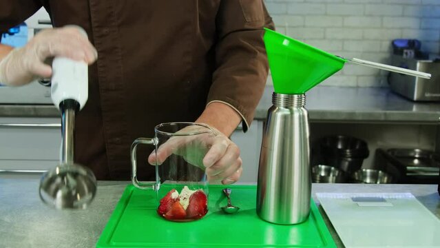 Chef prepares natural strawberry smoothie in glass measuring cup. Man crafts delectable sauce for fish using kitchen appliances