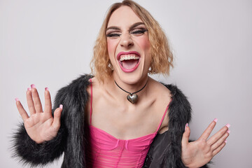 Horizontal shot of cheerful transgender woman with bob hairstyle keeps palms raised up laughs...