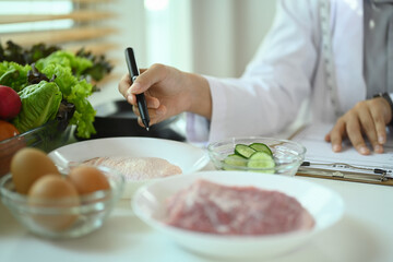 Nutritionist in white coat working at desk with protein sources and vegetables